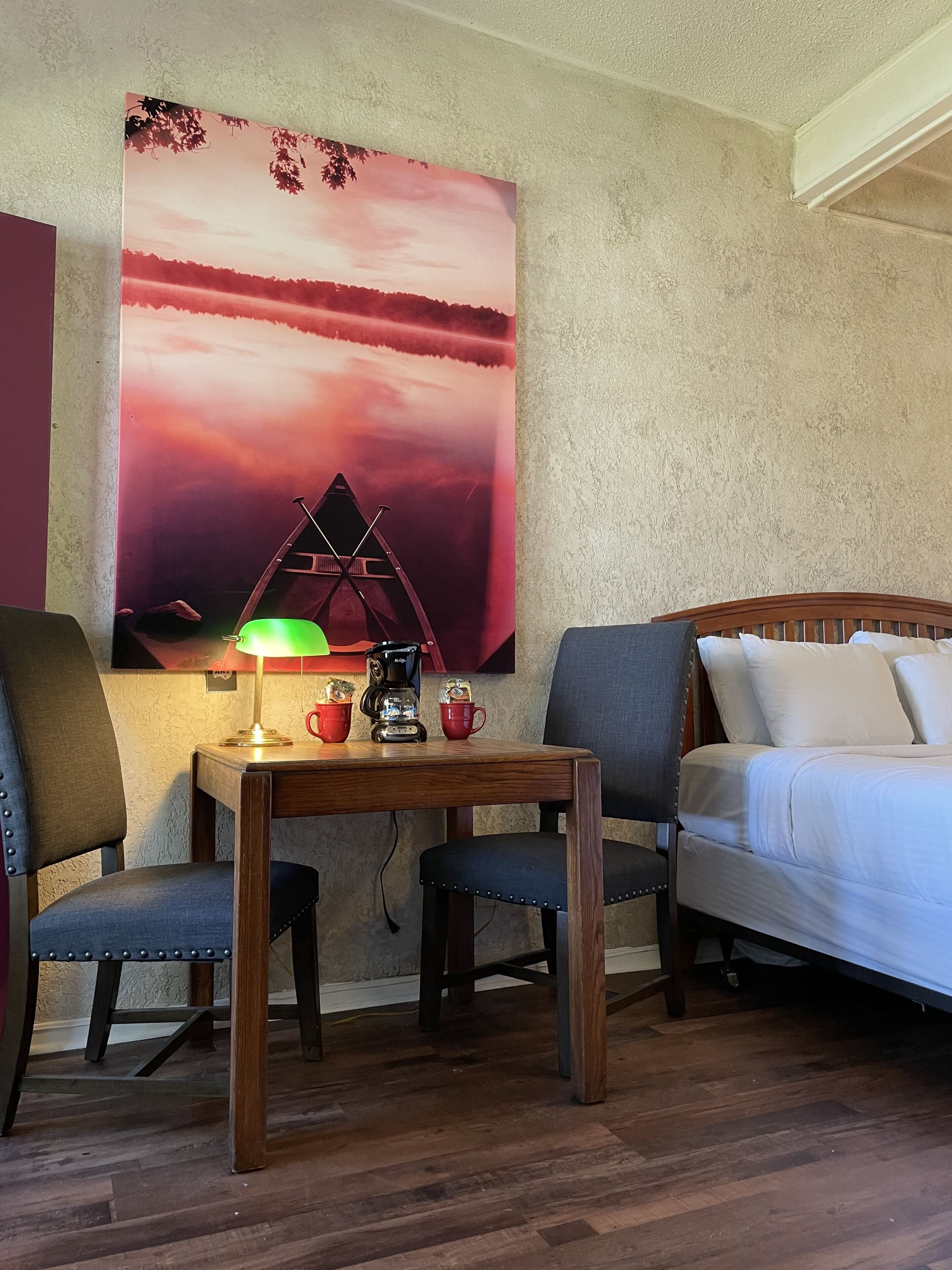 A cozy room with a wooden table, two chairs, a bed, and a large abstract painting on the wall.