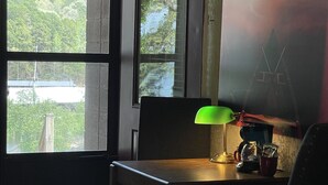A hotel room with a bed, a desk with a lamp, a chair, a window with a view of trees, and a painting on the wall. - Mountain Harbor Queen Guest Room on Lake Ouachita by RedAwning (Mount Ida)