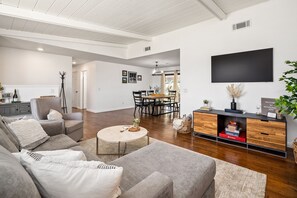 A modern living room with a sofa, coffee table, and a dining area with chairs and a table.