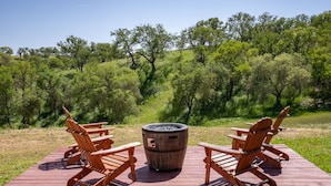 Una terraza de madera con cuatro sillas Adirondack y un estufa de leña en el centro.