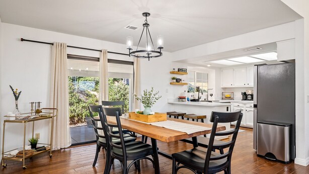 Una cocina moderna con armarios blancos, un refrigerador de acero inoxidable y un comedor con una mesa de madera y sillas negras.