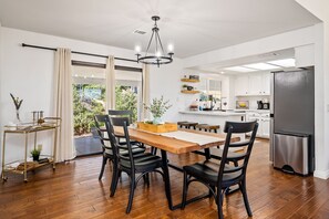A modern kitchen with white cabinets, a stainless steel refrigerator, and a dining area with a wooden table and black chairs.