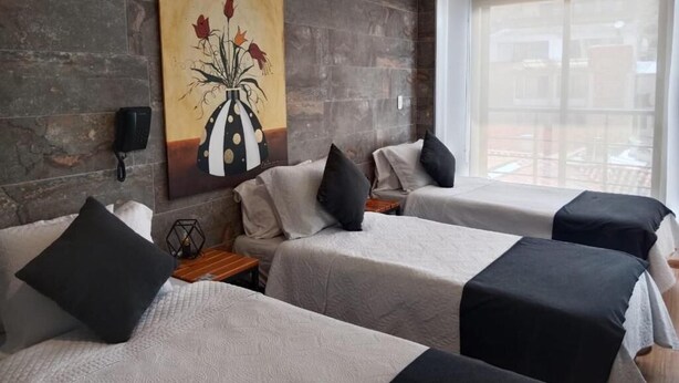 A hotel room with two beds, a large window, a stone wall, and a painting of flowers. - Hotel Posada Santa Elena (Tunja)