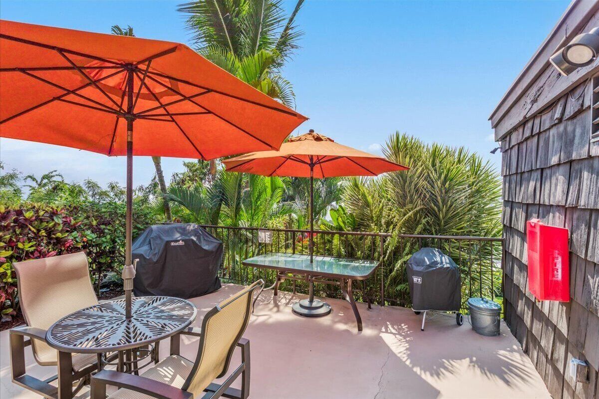 Un patio con una mesa, sillas, dos sombrillas, una parrilla y un basurero.