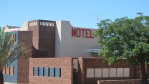 Um motel com fachada de tijolos, uma grande placa com a palavra "MOTEL" e uma árvore em primeiro plano.