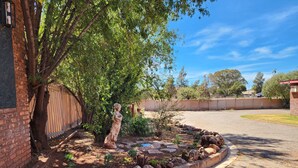 Um jardim com uma estátua, um muro de tijolos e uma área cercada.