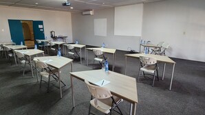 Uma sala de conferências com várias mesas e cadeiras, um projetor e uma lousa.