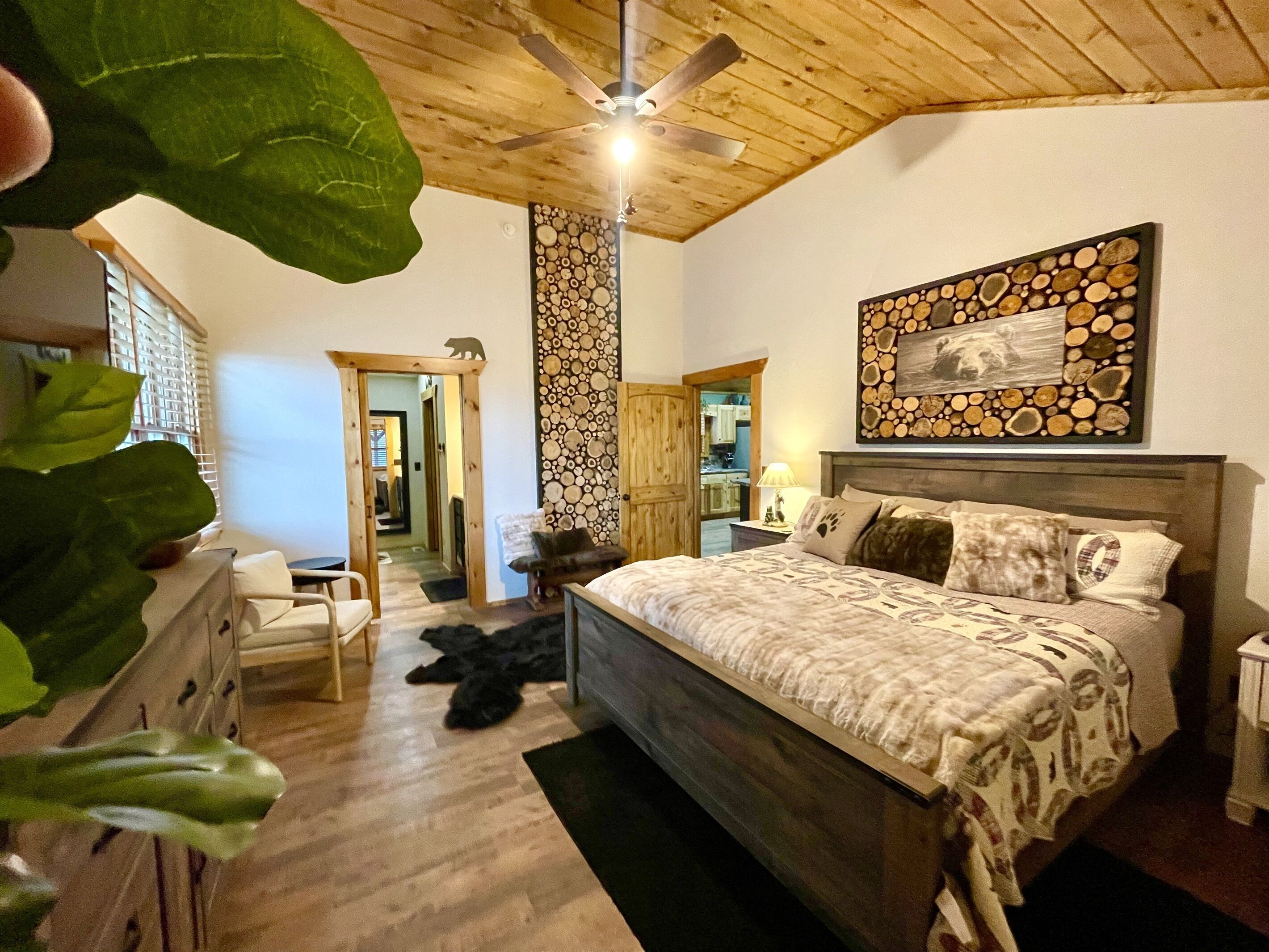Une chambre avec un plafond en bois, un lit recouvert d’une literie à motifs, un tableau accroché au mur et un plancher en bois.