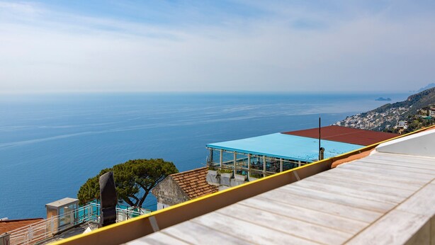 Vista costeira de um ponto elevado, com mar azul cristalino e uma linha de costa distante com edifícios.