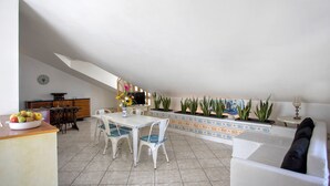 Uma sala de jantar com mesa e cadeiras brancas, uma cesta de frutas e um relógio na parede.