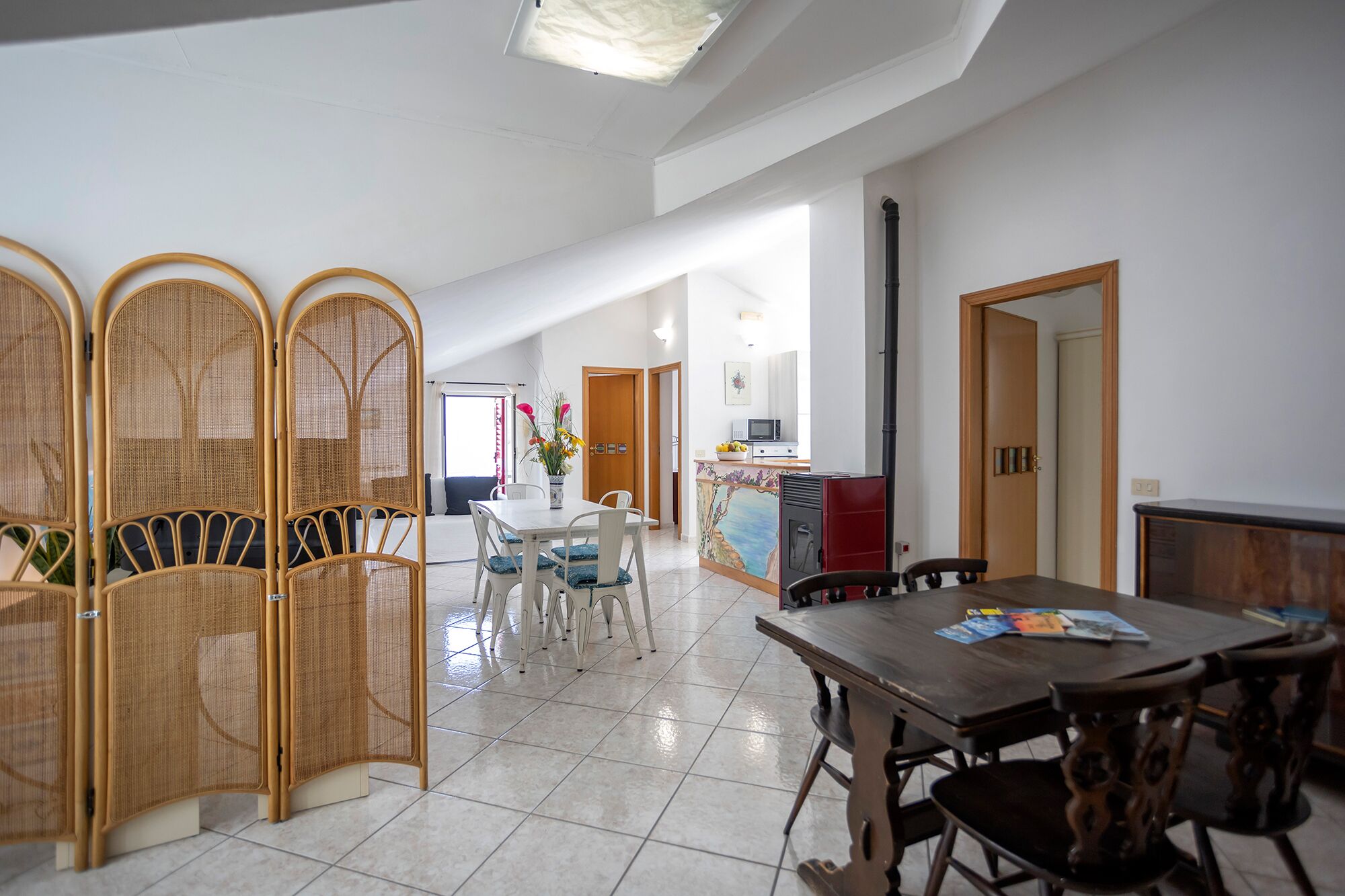 Un'ampia zona giorno con tavolo da pranzo, sedie, angolo cottura e un pannello decorativo.