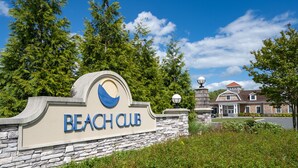 Señal de Beach Club, con un muro de piedra y un edificio al fondo.