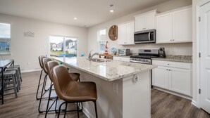 Una cocina moderna con armarios blancos, encimera de granito y una isla central con taburetes de bar.