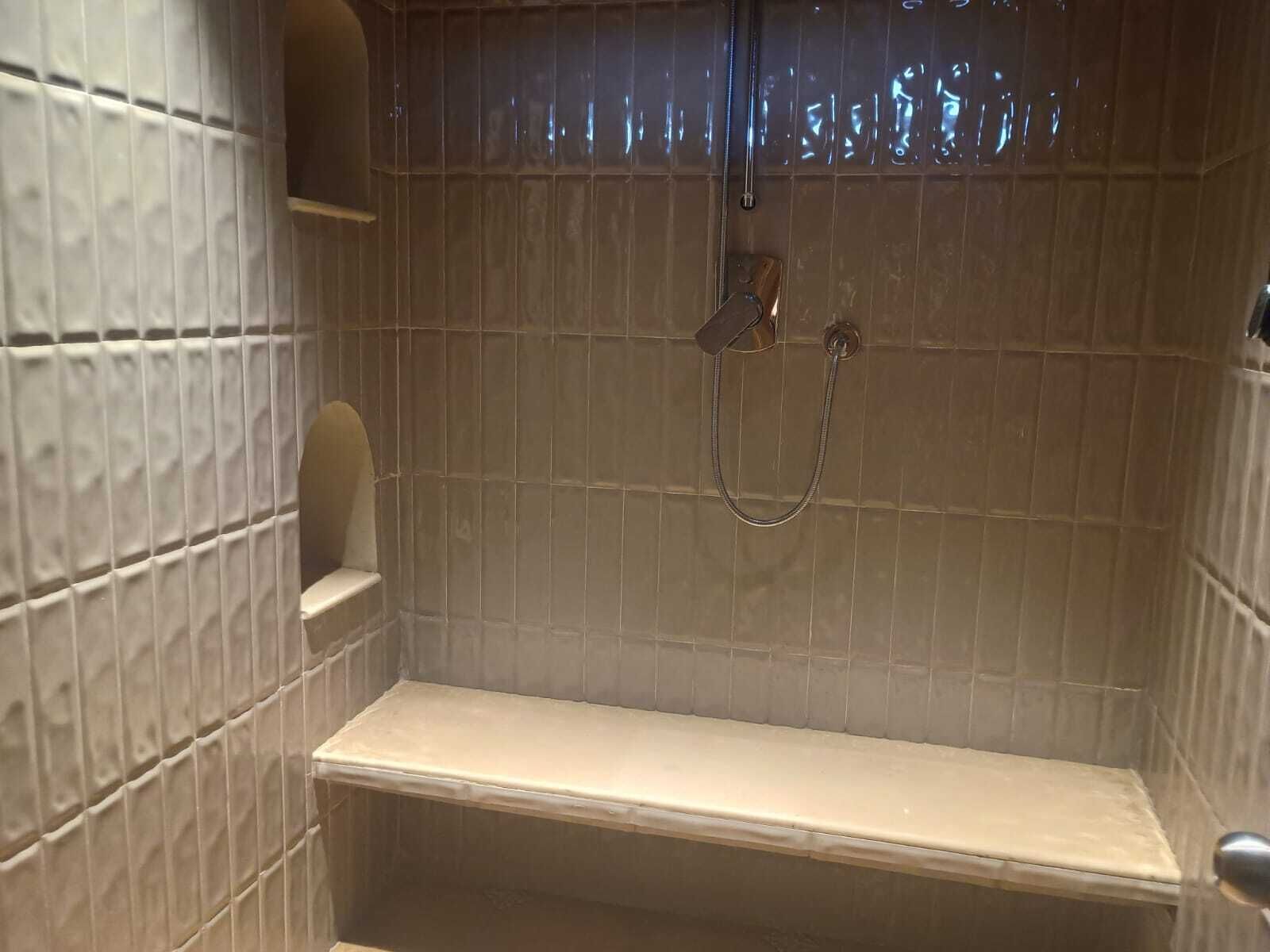 Une petite cabine de douche carrelée, dotée d’une seule étagère et d’un pommeau de douche à main.