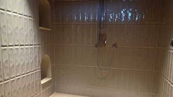 A small, tiled shower stall with a single shelf and a handheld showerhead.