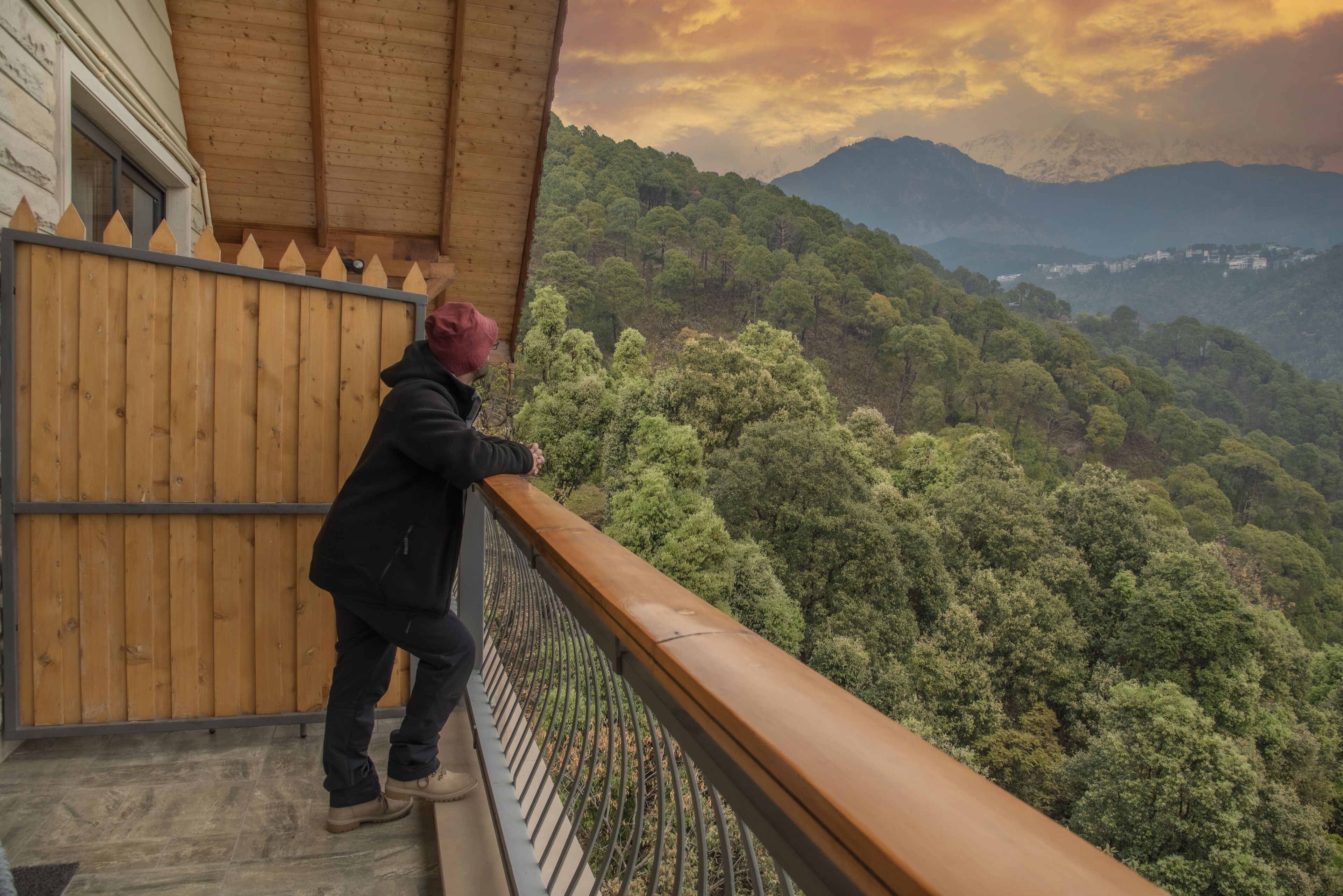 Eine Person steht auf einem Balkon mit Blick auf einen bewaldeten Gebirgszug.