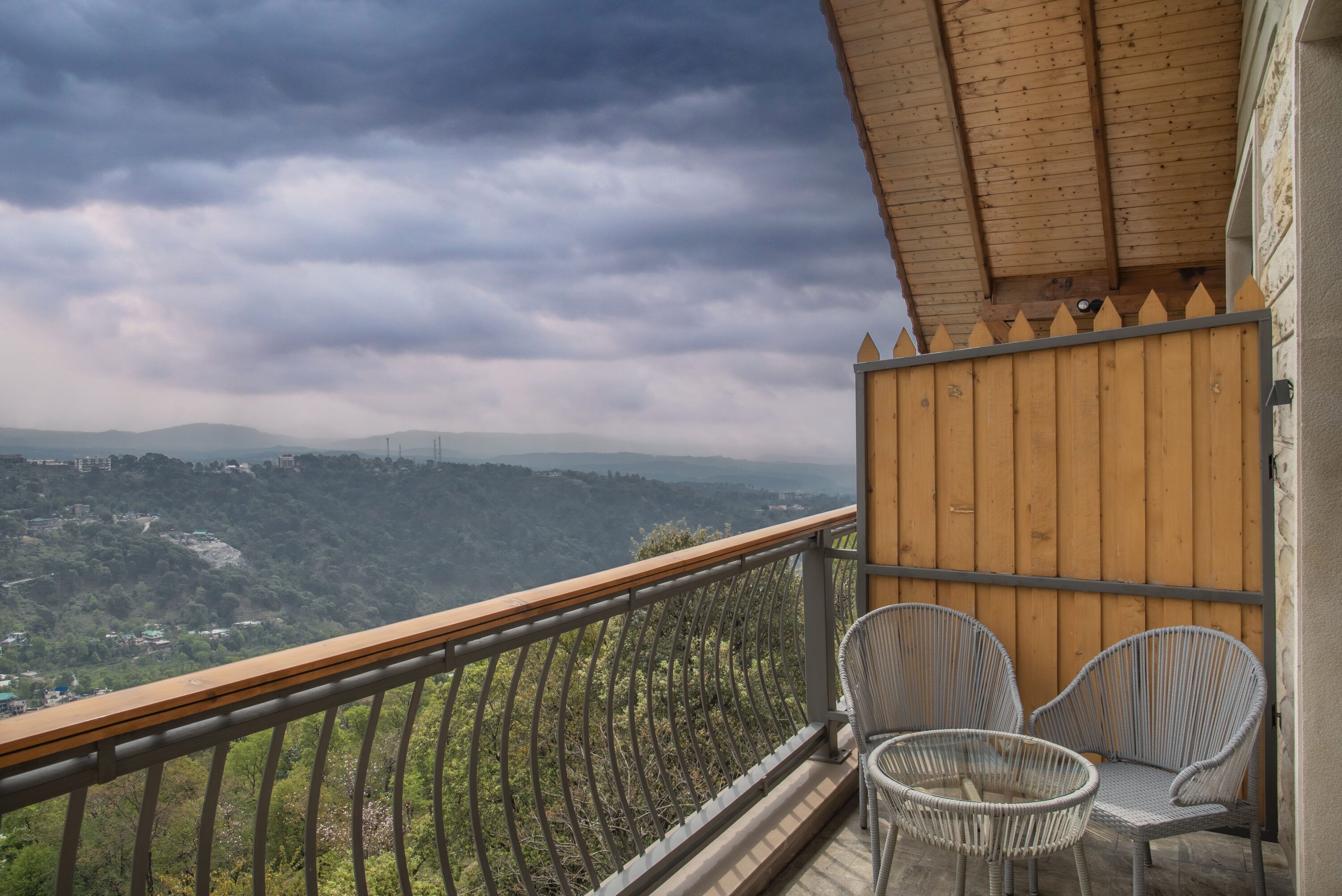 Un balcon donnant sur un paysage montagneux, deux fauteuils en osier et une clôture en bois.