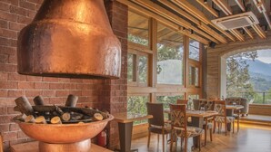 Un interior rústico con un gran hogar de cobre, mesas y sillas de madera, y vistas al exterior.