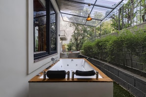 Un baño moderno con una bañera grande, una ventana y un espacio exterior cubierto de cristal.