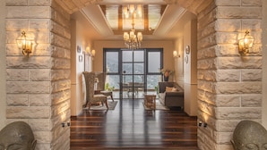 Amplia habitación con piso de madera, paredes de piedra, un candelabro y un ventanal con vistas.