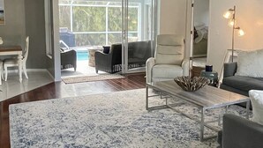 A spacious living room with a ceiling fan, a large window, and a view of a pool.