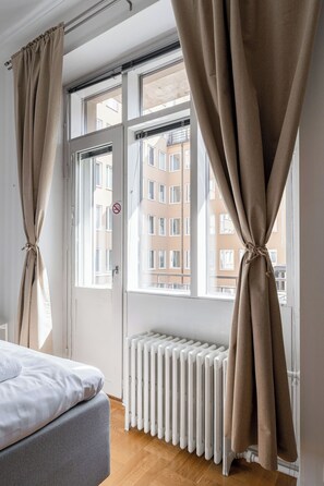 Een kamer met een bed, een radiator en een raam met teruggebonden gordijnen.