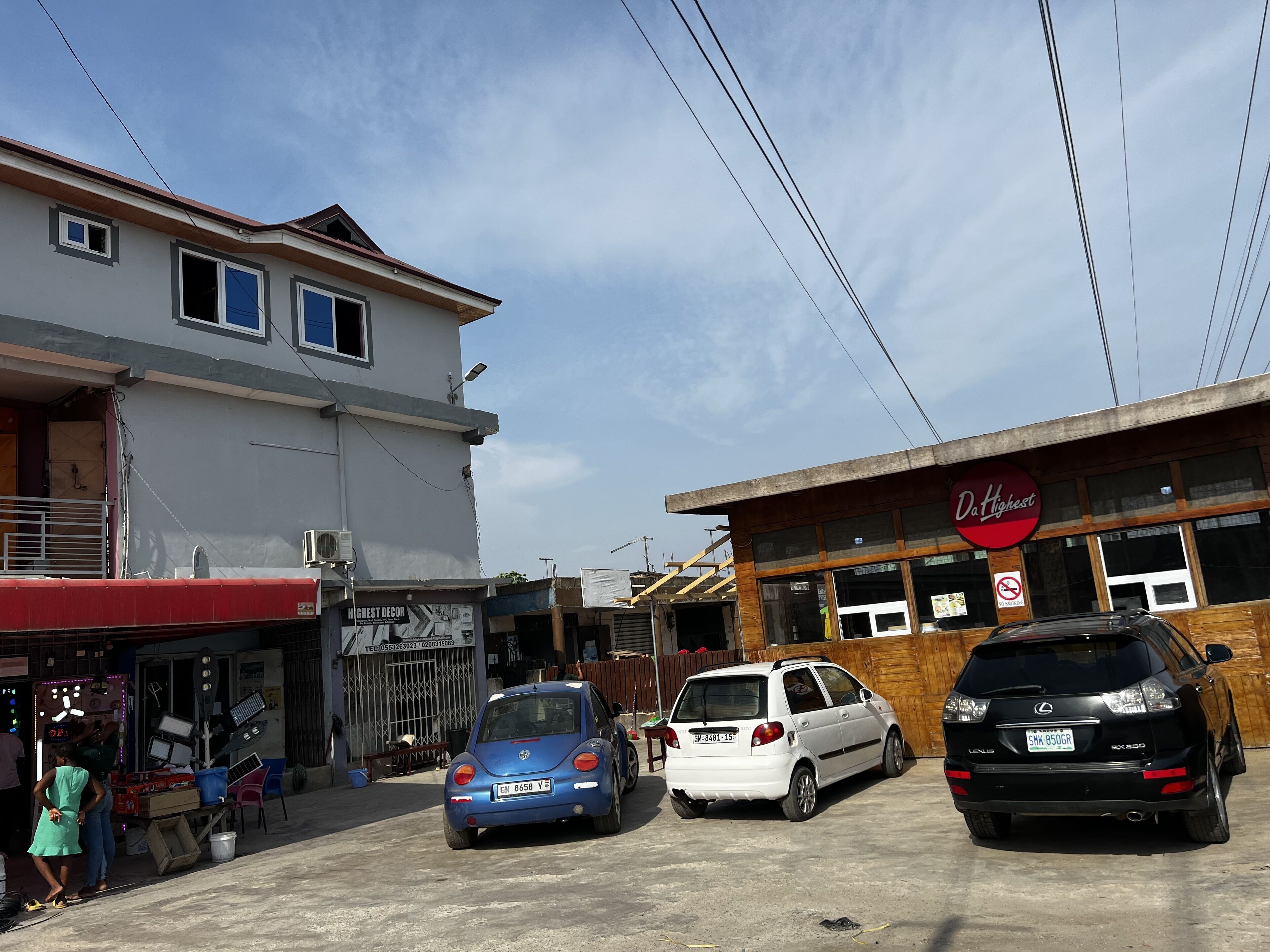 A parking area with three cars parked in front of a building with a sign reading "Da'Highest".