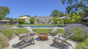 A backyard with a fire pit, lounge chairs, and a pool.