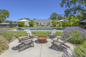A backyard with a fire pit, lounge chairs, and a pool.