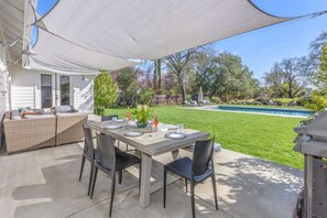 Een terras met een eettafel, uitkijkend op een achtertuin met een zwembad en ligbedden.