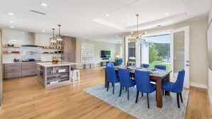 A modern kitchen with wooden cabinets, a central island, and a dining area with blue chairs and a wooden table.