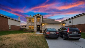 A two-story house with a garage, two cars parked in front, and a well-maintained lawn.
