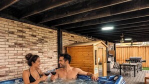 A couple in a hot tub with a wooden sauna and outdoor grill area. - Elite 5BR/3.5B Home with Game Room & Sauna (Grand Prairie)