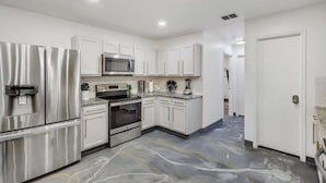 A modern kitchen with stainless steel appliances, white cabinetry, and a marble floor. - Elite 5BR/3.5B Home with Game Room & Sauna (Grand Prairie)