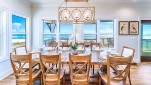 A dining area with a wooden table and chairs, a chandelier, and large windows with a view of the beach. - Stella Maris- GULF FRONT 7BR/7BA House with private heated POOL, Views from every room (Mexico Beach)