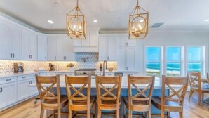 A spacious kitchen with white cabinets, a central island with bar stools, and two pendant lights. - Stella Maris- GULF FRONT 7BR/7BA House with private heated POOL, Views from every room (Mexico Beach)