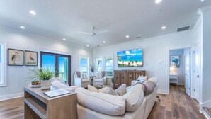 A spacious living room with a large sectional sofa, a wooden coffee table, and a TV mounted on the wall. - Stella Maris- GULF FRONT 7BR/7BA House with private heated POOL, Views from every room (Mexico Beach)