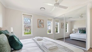 Une chambre avec un grand lit, un ventilateur de plafond, un miroir et une vue sur une autre pièce.