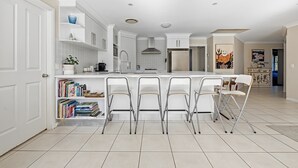 Une cuisine moderne avec des meubles blancs, un îlot central doté de tabourets de bar et une bibliothèque remplie de livres.
