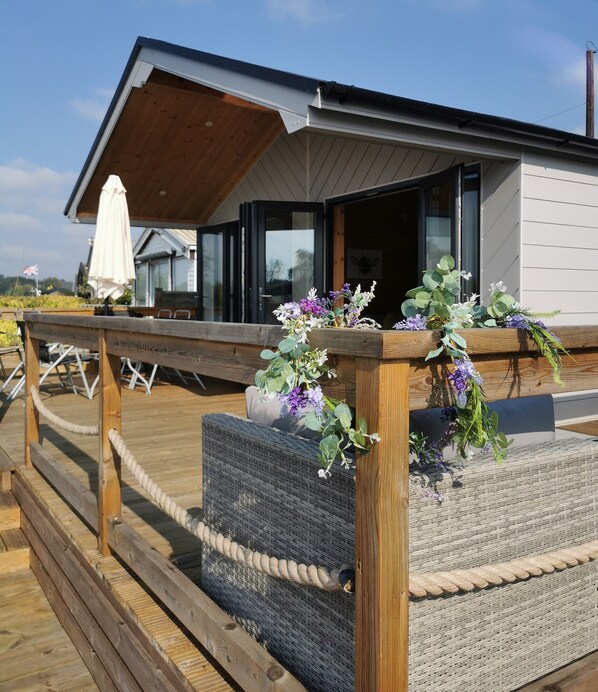 A wooden deck with outdoor seating and a railing, overlooking a modern building with large windows.