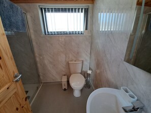 A compact bathroom with a toilet, a small trash bin, a window with bars, and a sink with a mirror.