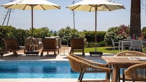 A poolside area with lounge chairs, umbrellas, and a dining table. - Casa Girassol, villa wih private pool at Algarve Clube Atlântico (Carvoeiro)