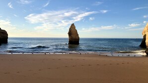 A beach with a prominent rock formation in the water, a sandy shore, and a clear sky. - Casa Girassol, villa wih private pool at Algarve Clube Atlântico (Carvoeiro)