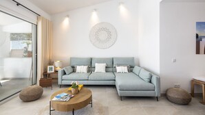 A modern living room with a grey sectional sofa, a round wooden coffee table, and a large decorative wall piece. - Casa Girassol, villa wih private pool at Algarve Clube Atlântico (Carvoeiro)