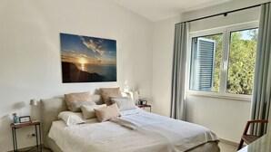 A bedroom with a bed, a nightstand, a lamp, a painting, and a window with curtains. - Casa Girassol, villa wih private pool at Algarve Clube Atlântico (Carvoeiro)