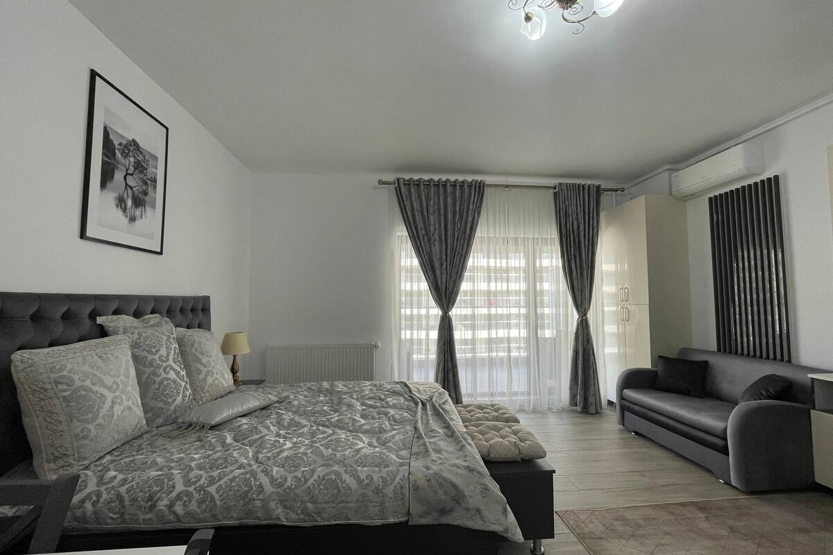 Un dormitorio moderno con una cama grande, un sofá, una mesita auxiliar y un cuadro enmarcado en la pared.