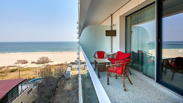 A balcony with a view of the beach and ocean. There are wicker chairs with red cushions and a table. - Grup Casa Del Mar (Năvodari)