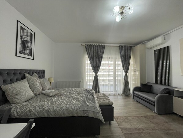 A bedroom with a bed, a sofa, a radiator, and a window with curtains.