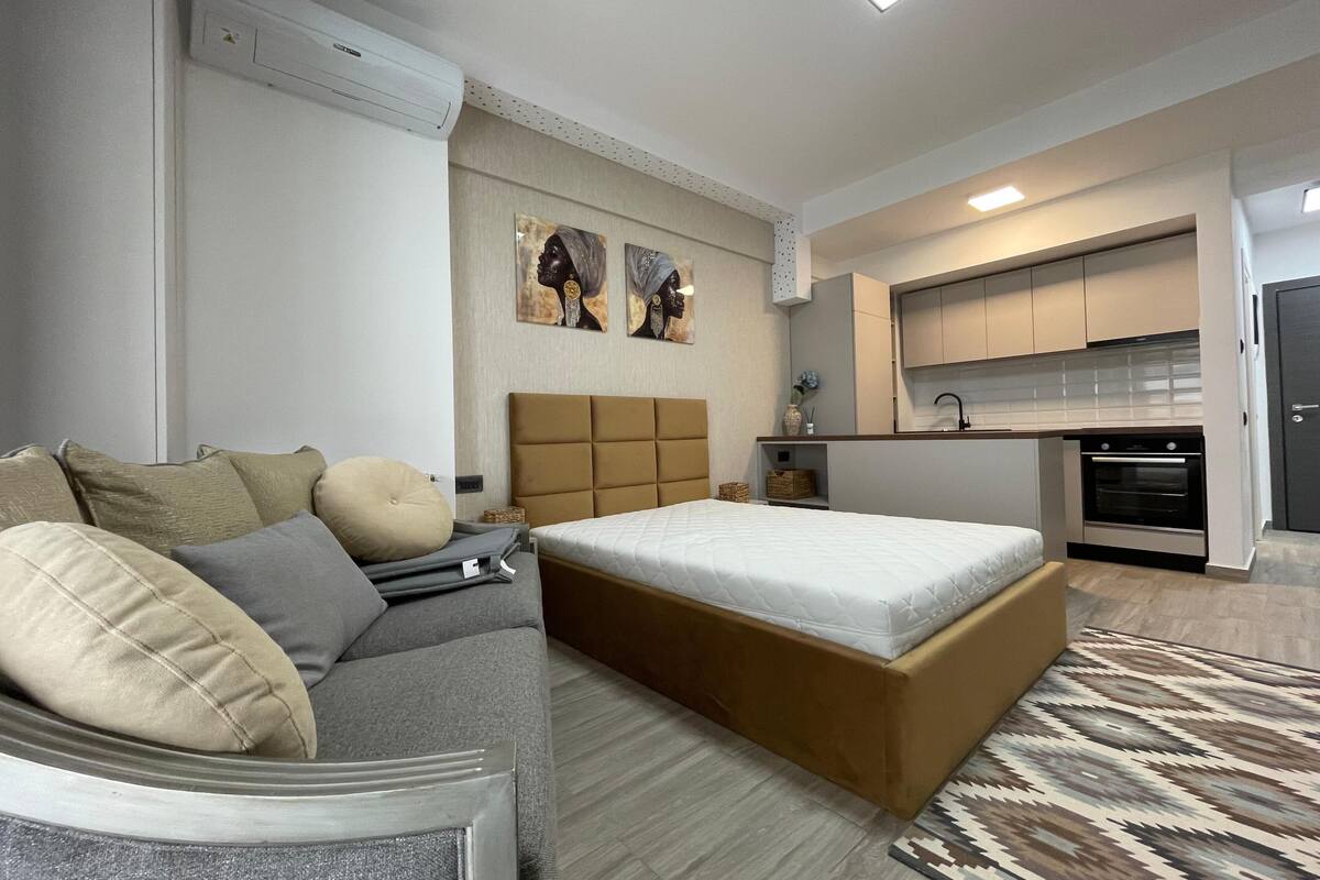 Un dormitorio moderno con sofá, cama grande, kitchenette y obras de arte en la pared.