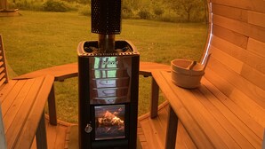 Un estufa de leña con puerta de vidrio, una chimenea de metal y una base de piedra, ubicada en una terraza de madera con bancos.
